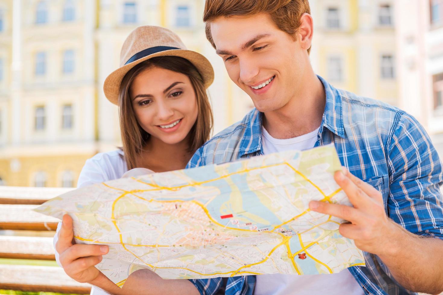 escolhendo um bom lugar para visitar. feliz casal jovem turista sentado no banco juntos e examinando o mapa foto