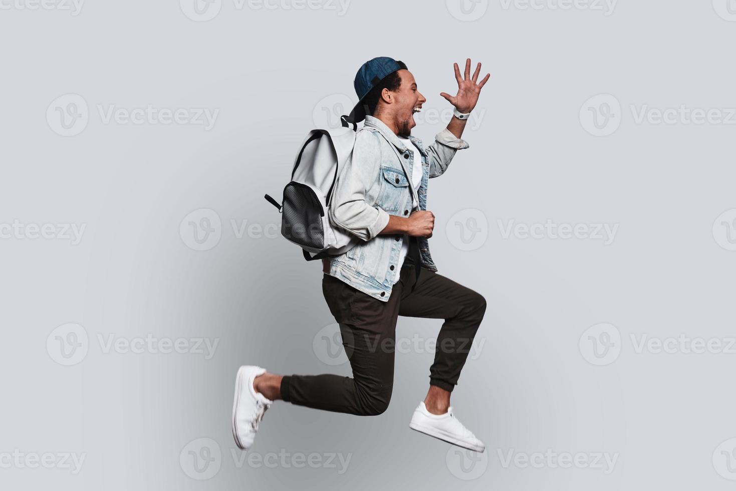 feliz. jovem bonito em roupas casuais, sorrindo e gesticulando enquanto pulava contra um fundo cinza foto