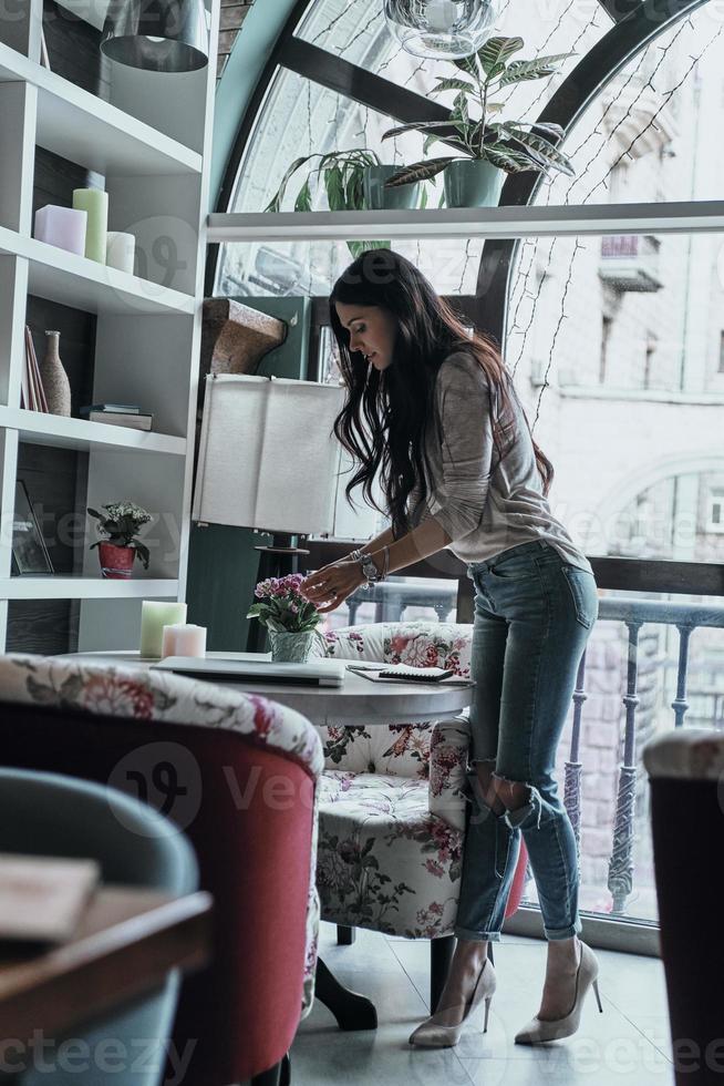 tudo deve ser perfeito. comprimento total da bela jovem ajustando flores na mesa em pé no restaurante foto