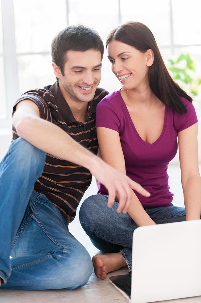 navegando na net juntos. lindo casal jovem trabalhando juntos no laptop enquanto homem apontando o monitor e sorrindo foto