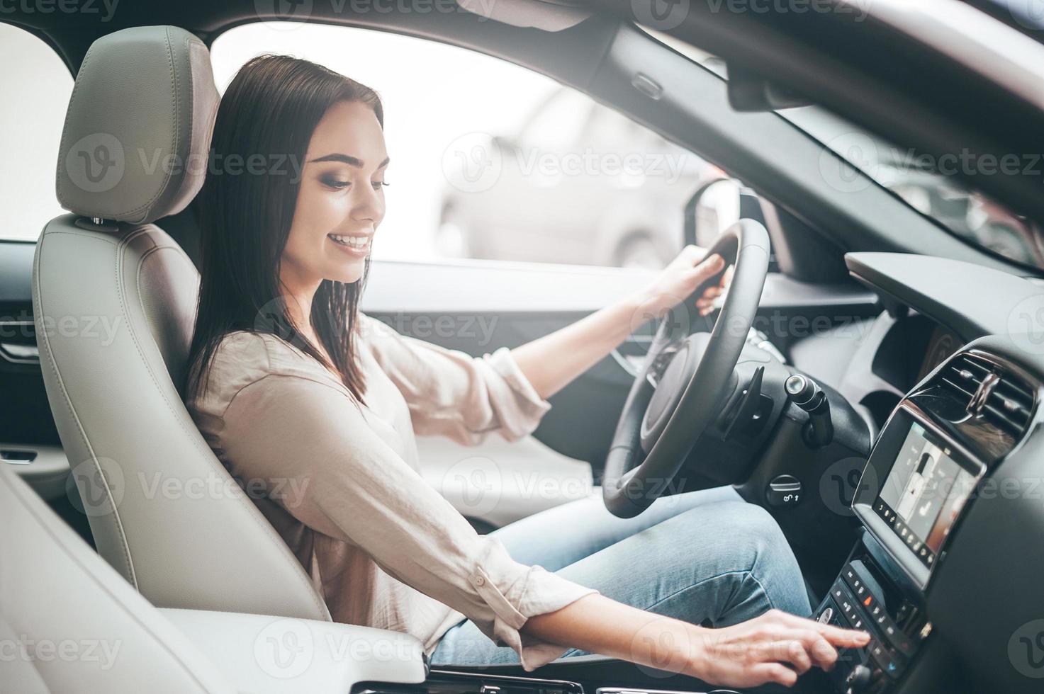 em busca de músicas favoritas. jovem mulher atraente sorrindo e apertando botões enquanto dirige um carro foto