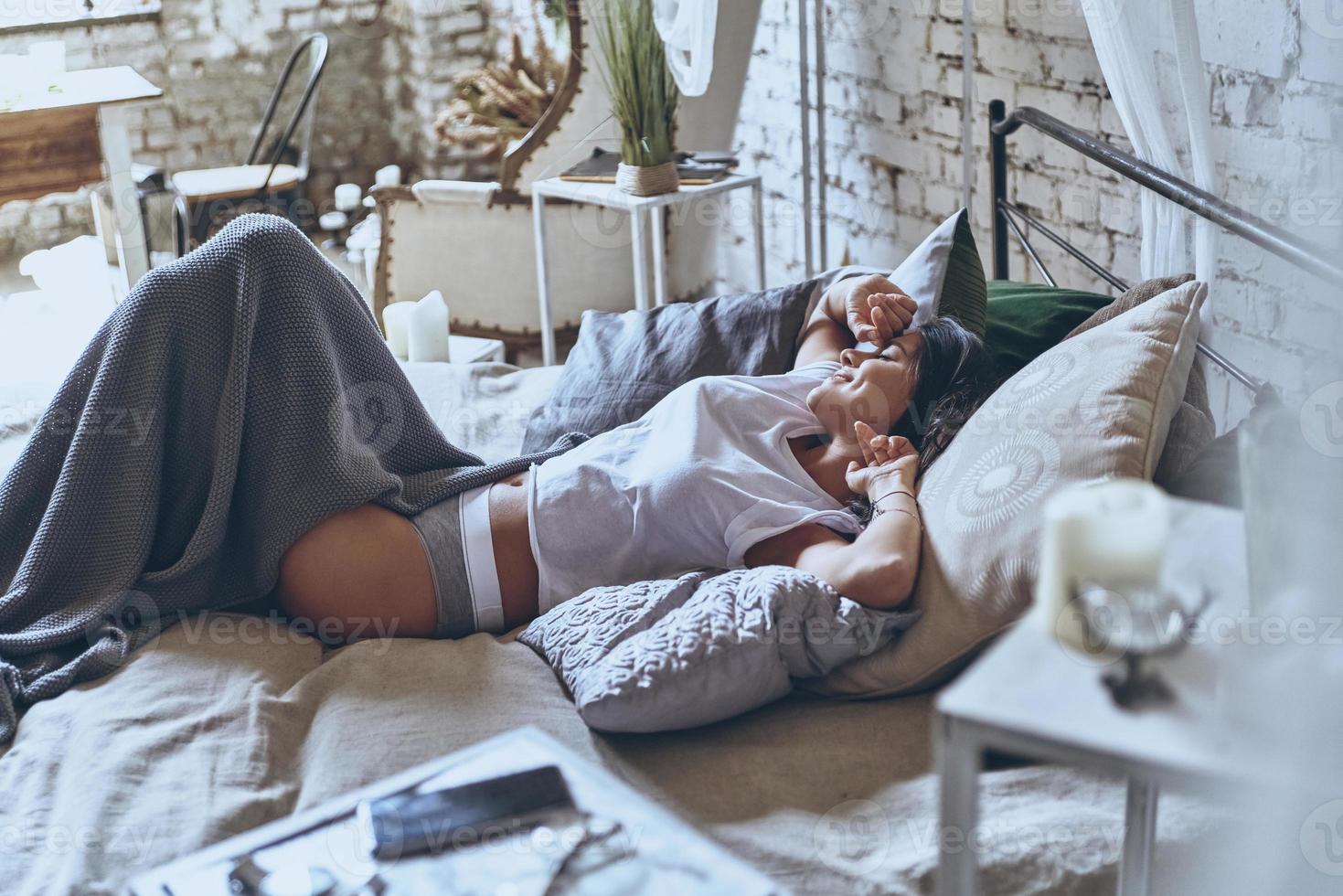 Grande manhã. mulher jovem e atraente, mantendo os olhos fechados e sorrindo enquanto estava deitado na cama em casa foto