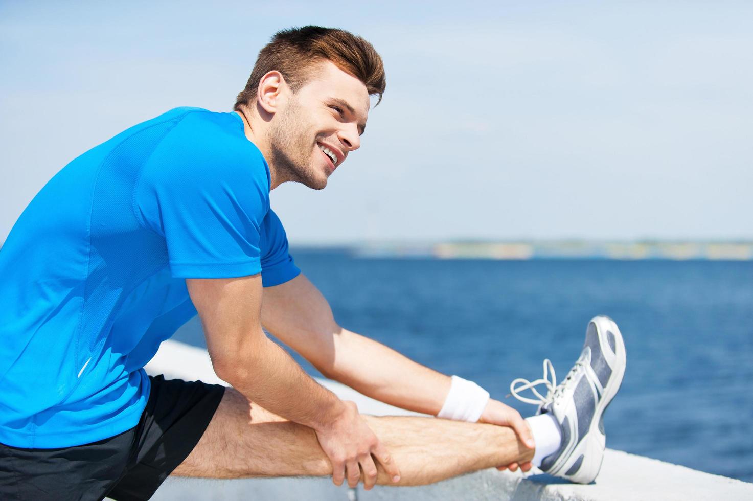 alongamento antes de correr. jovem bonito fazendo exercícios de alongamento e sorrindo em pé ao ar livre foto