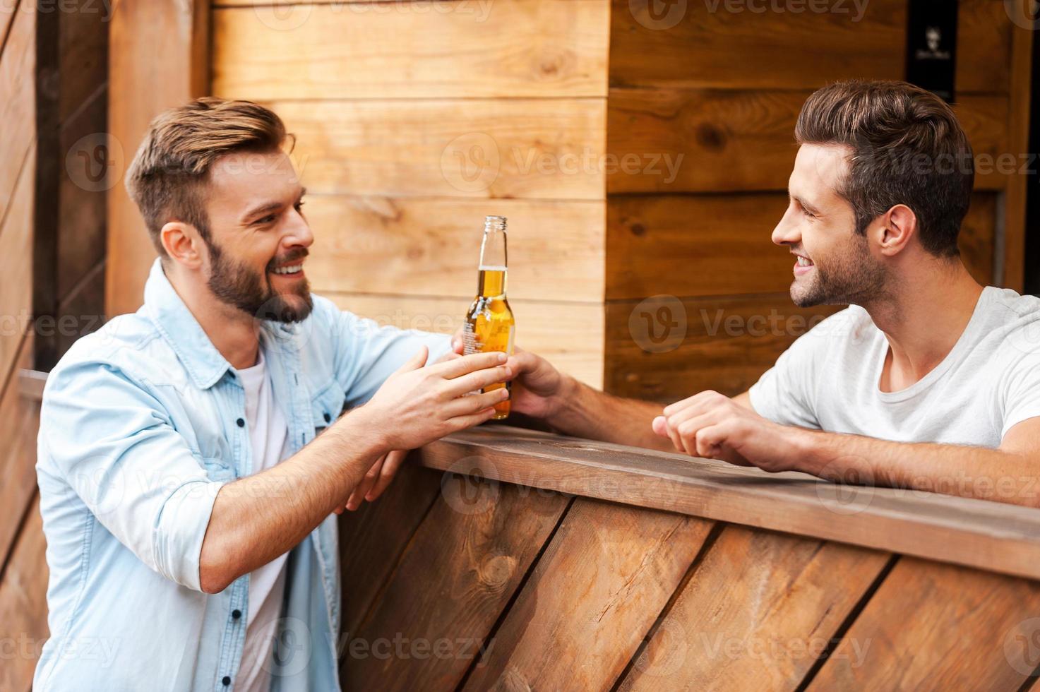 aqui está a sua cerveja jovem barman feliz dando uma garrafa de cerveja para seu cliente em pé no balcão do bar foto