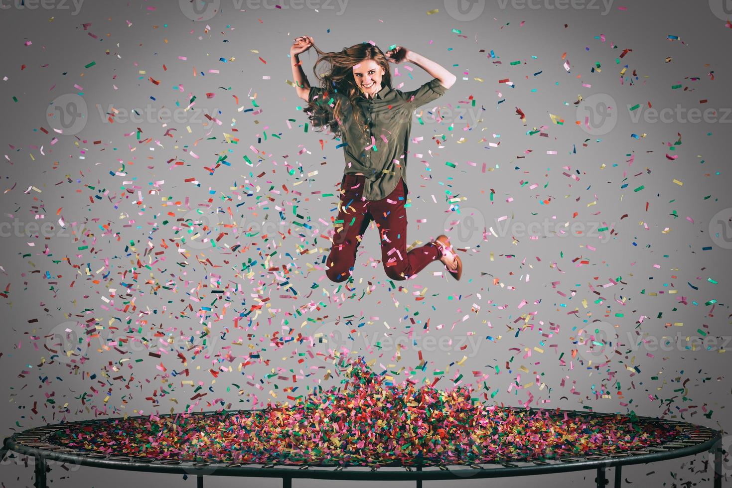 diversão colorida. tiro no ar da bela jovem pulando no trampolim com confete ao redor dela foto