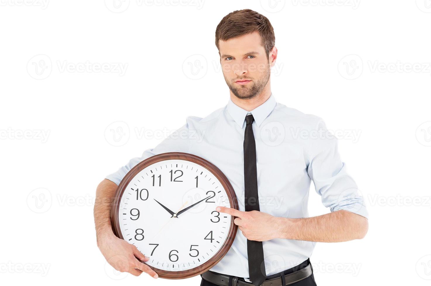 tempo é dinheiro jovem sério em trajes formais, segurando um relógio na mão e apontando-o enquanto está isolado no fundo branco foto