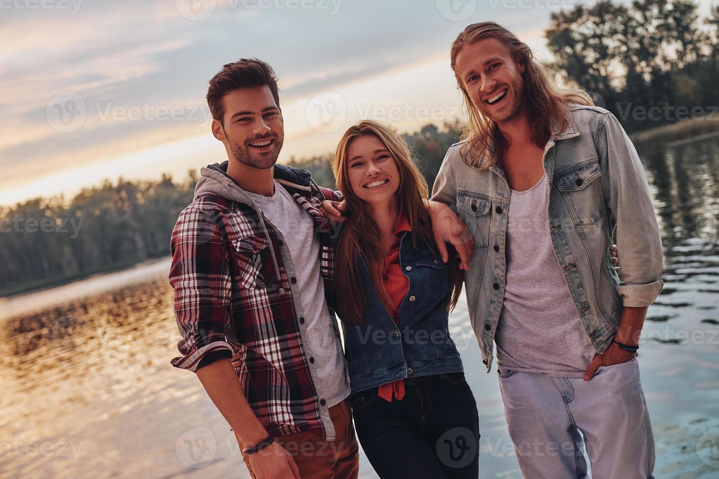 sentindo-se aconchegados juntos. grupo de jovens em roupas casuais sorrindo e olhando para a câmera em pé perto do lago foto