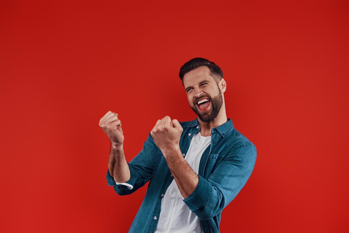 encantador jovem em roupas casuais, fazendo uma careta e gesticulando em pé contra um fundo vermelho foto