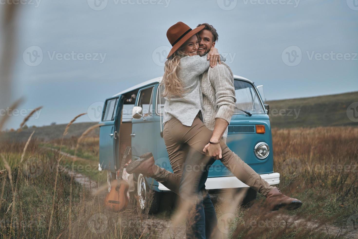 felicidade despreocupada. lindo casal jovem abraçando e sorrindo em pé perto da mini van azul estilo retrô foto