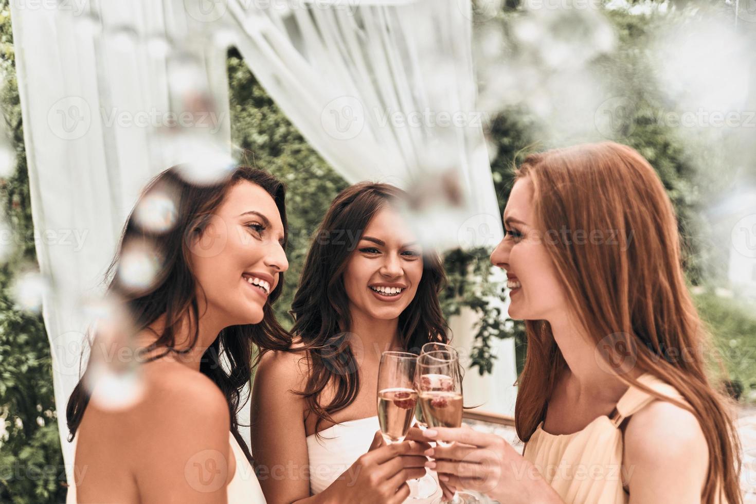 comemorando seu dia especial juntos. atraente jovem noiva brindando com champanhe com suas belas damas de honra em pé ao ar livre juntos foto