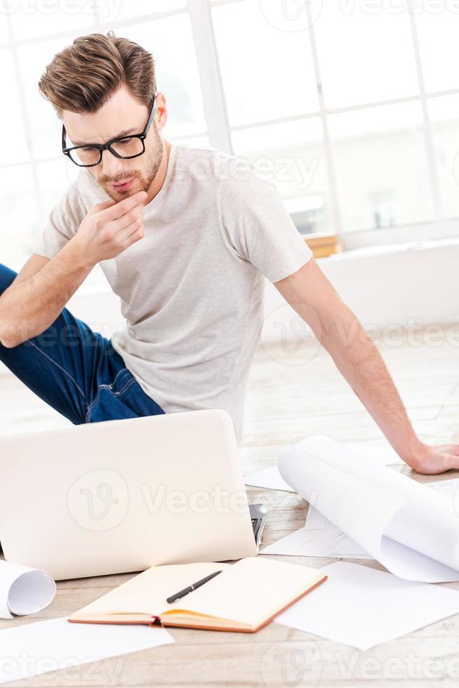 pensando em um novo projeto. jovem pensativo examinando a planta enquanto está sentado no chão em casa foto