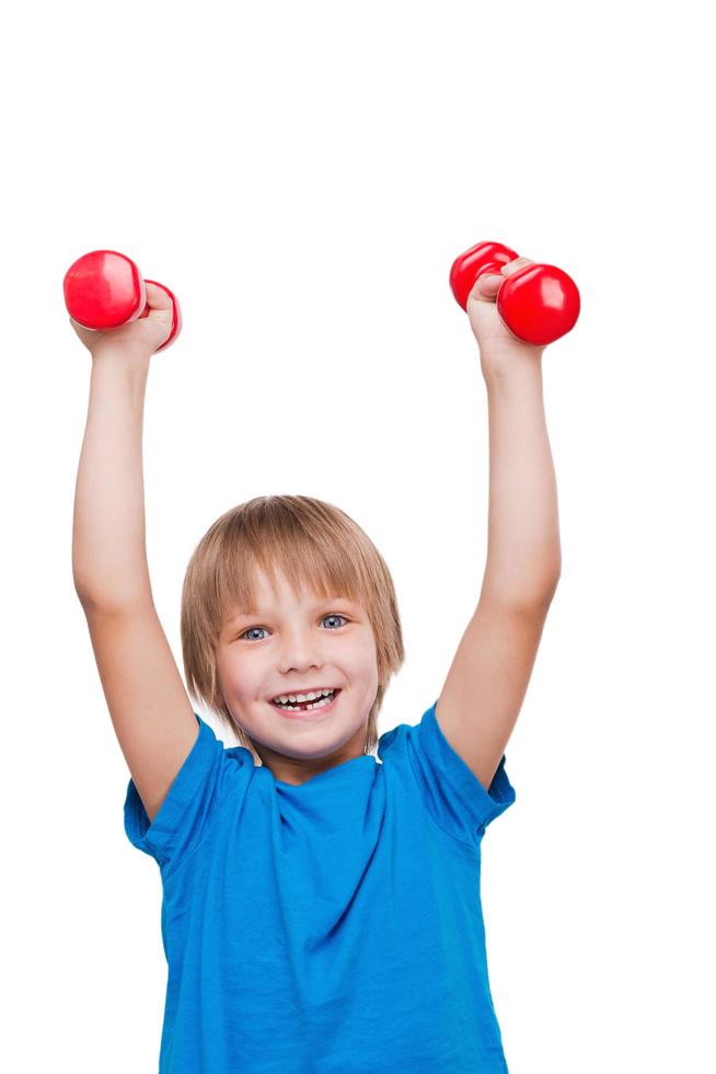 homenzinho forte. menino feliz olhando para a câmera e sorrindo enquanto se exercita com halteres e em pé isolado no branco foto