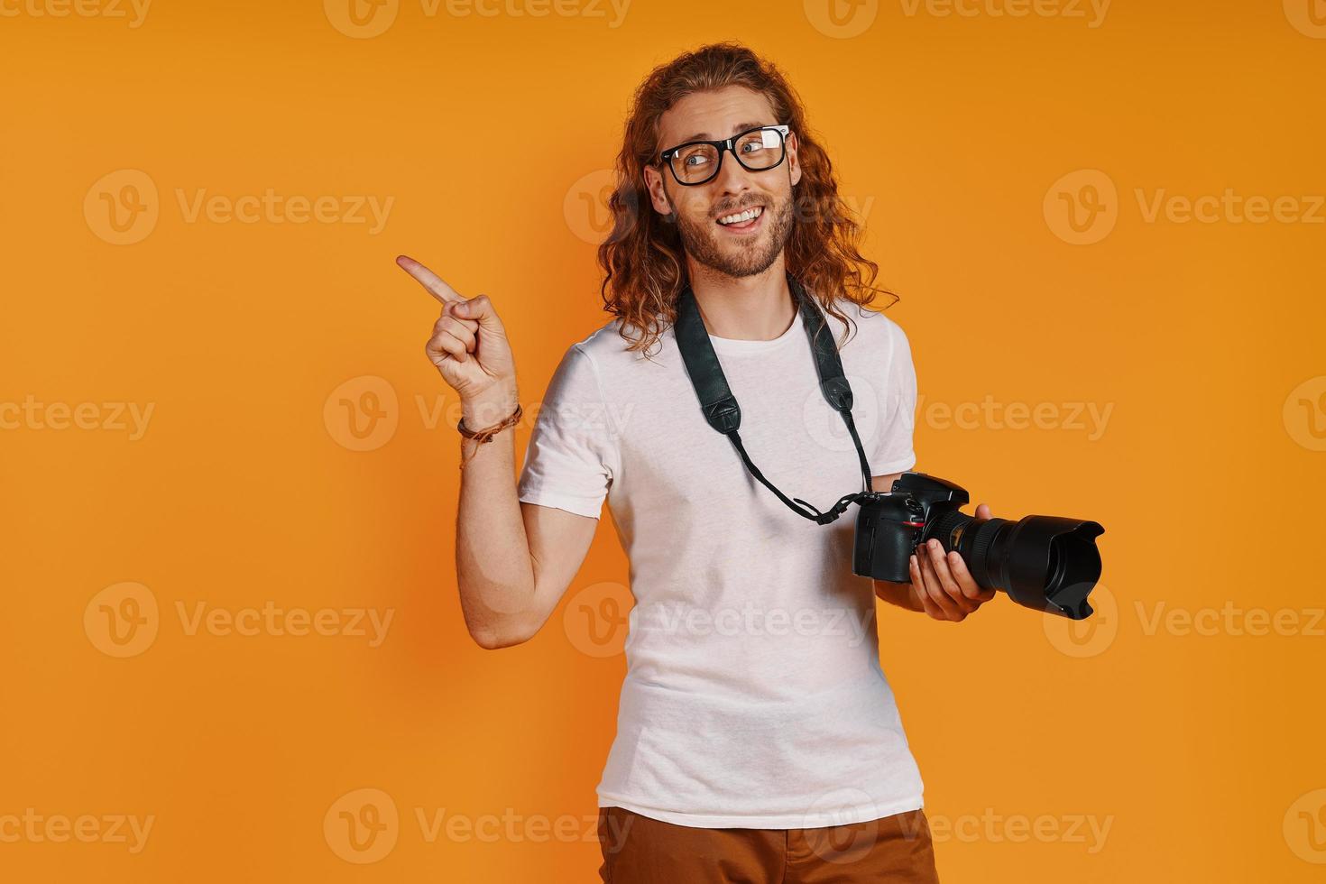 jovem feliz em roupas casuais, apontando o espaço da cópia e sorrindo em pé contra um fundo amarelo foto