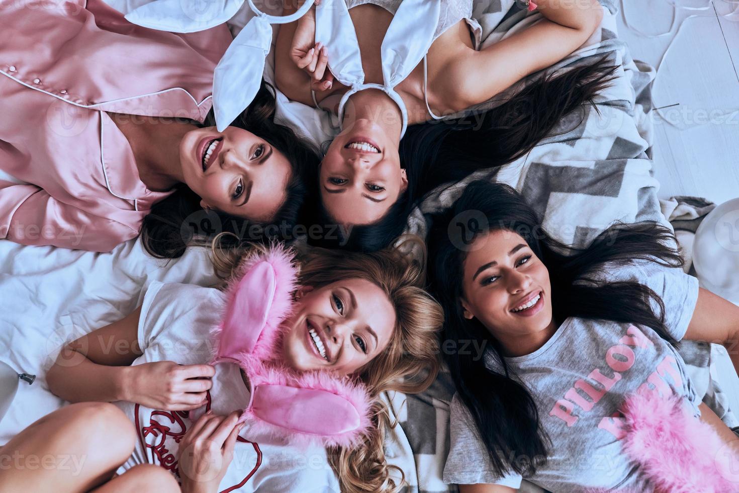 sempre juntos. vista superior de quatro mulheres jovens atraentes sorrindo enquanto estava deitado na cama em casa foto