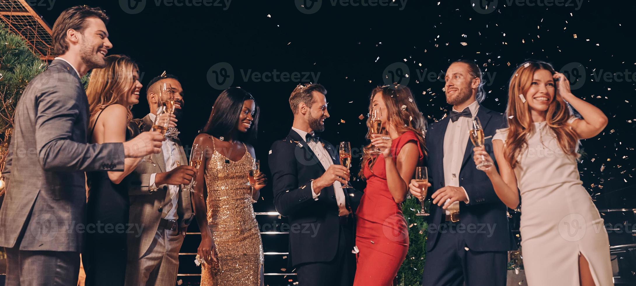 grupo de pessoas bonitas em trajes formais se comunicando e sorrindo enquanto passa o tempo na festa de luxo foto