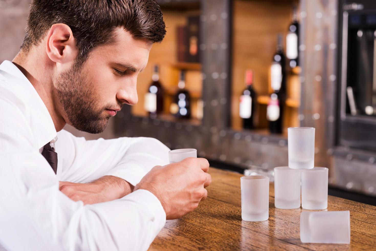 bebendo novamente. homem bêbado deprimido de camisa e gravata, encostado no balcão do bar e dormindo enquanto copos vazios em pé perto dele foto