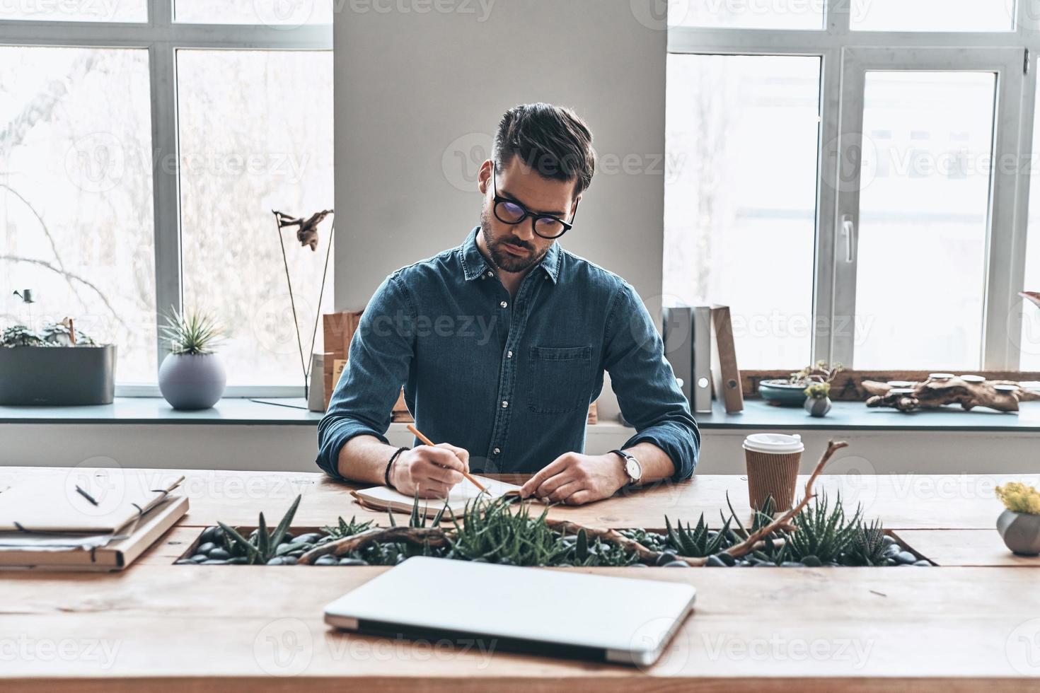 organizando cada minuto. jovem pensativo escrevendo algo no organizador pessoal enquanto está sentado no escritório foto