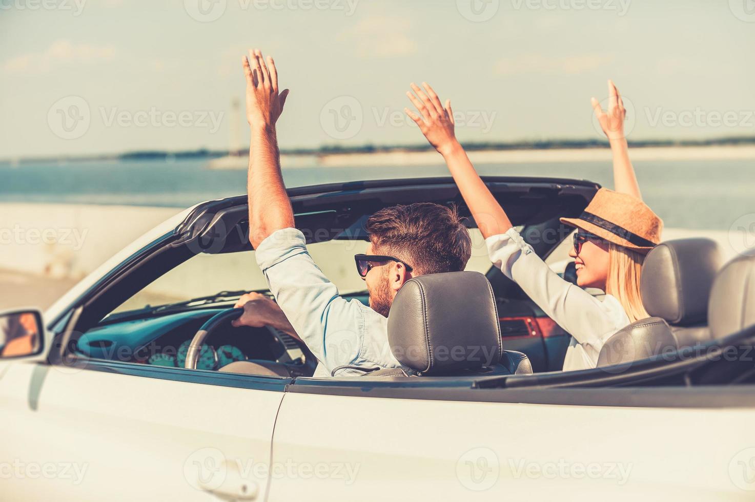 início perfeito de seu fim de semana. animado jovem casal mantendo os braços levantados enquanto andava em seu conversível branco foto