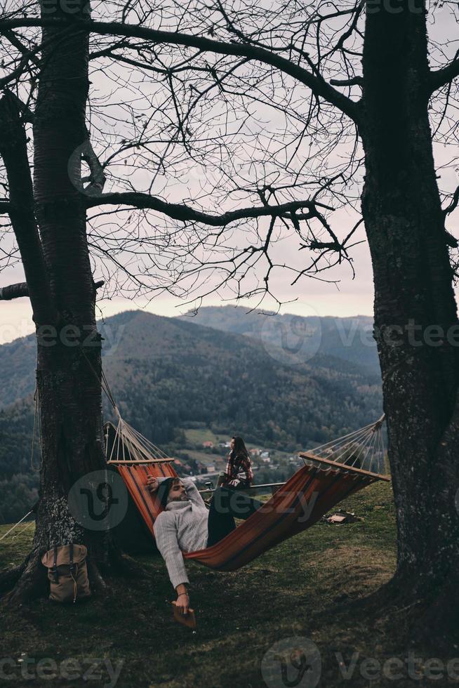 verdadeiro relaxamento. jovem bonito deitado na rede enquanto acampa com sua namorada foto