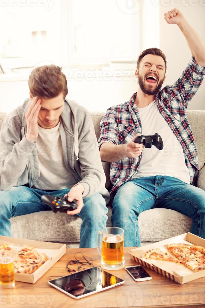 perdedores e vencedores. dois jovens jogando videogame enquanto está sentado no sofá foto