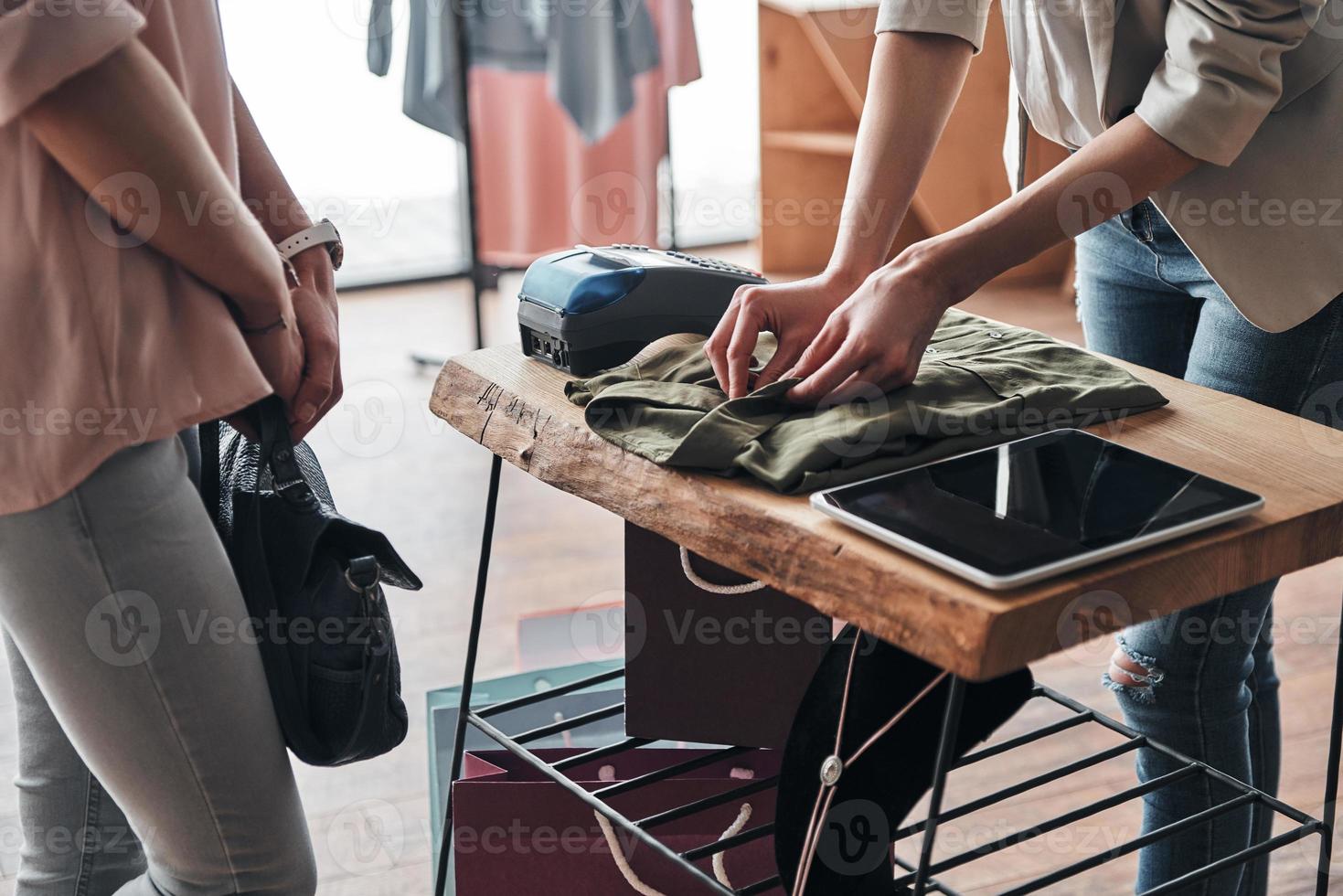 últimos detalhes. close-up de jovem dobrando uma camisa para seu cliente enquanto trabalhava na boutique de moda foto