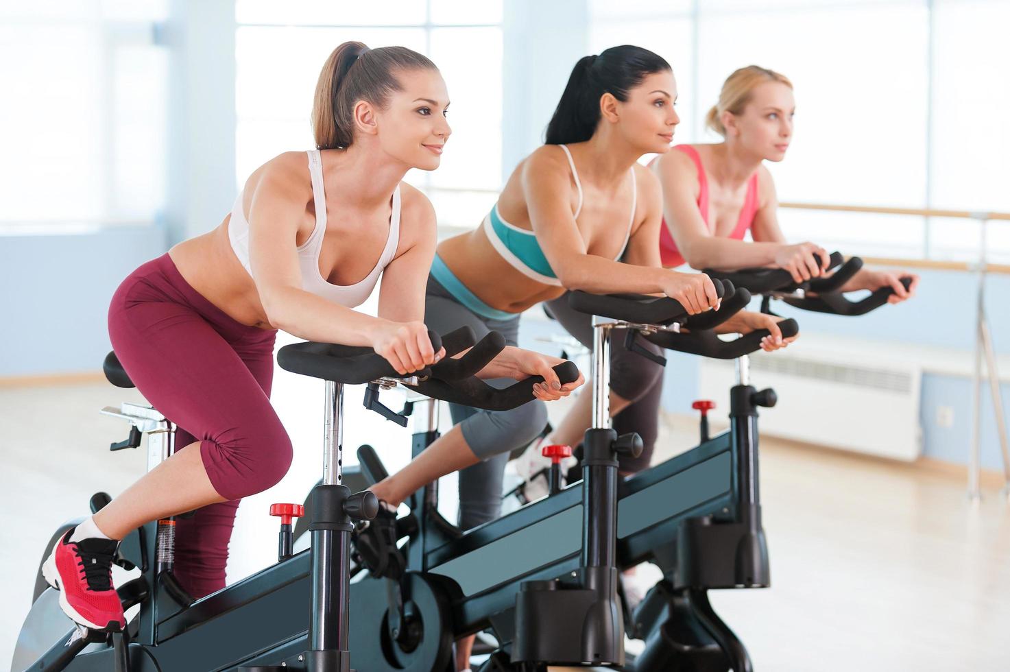 andar de bicicleta em bicicletas ergométricas. duas mulheres jovens atraentes em roupas esportivas se exercitando em bicicletas de ginástica foto