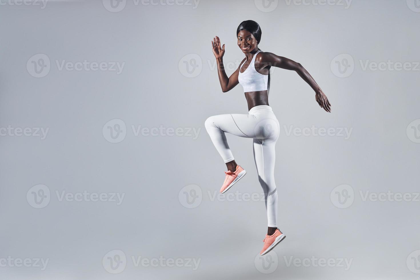comprimento total de uma jovem africana confiante em roupas esportivas pulando contra um fundo cinza foto