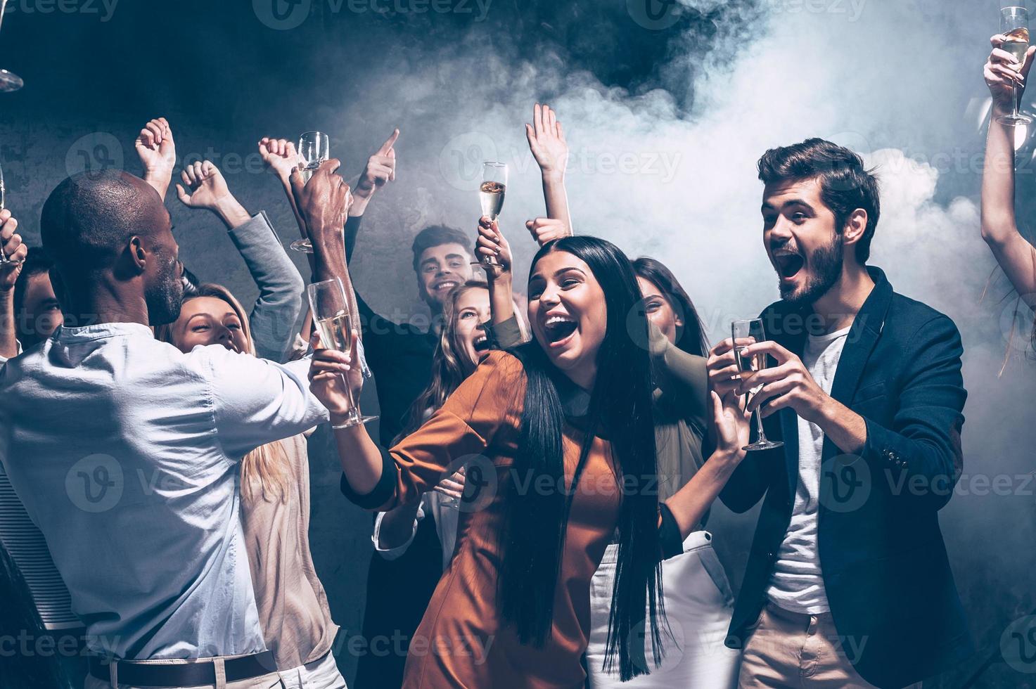 curtindo festa incrível. grupo de jovens bonitos dançando com taças de champanhe e parecendo feliz foto