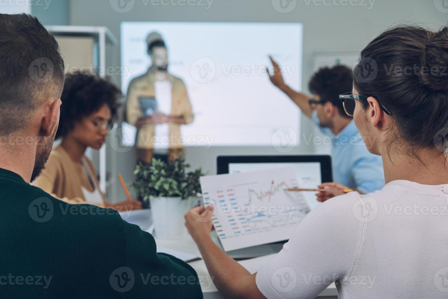 grupo de jovens modernos em roupas casuais inteligentes analisando dados na tela de projeção no escritório foto