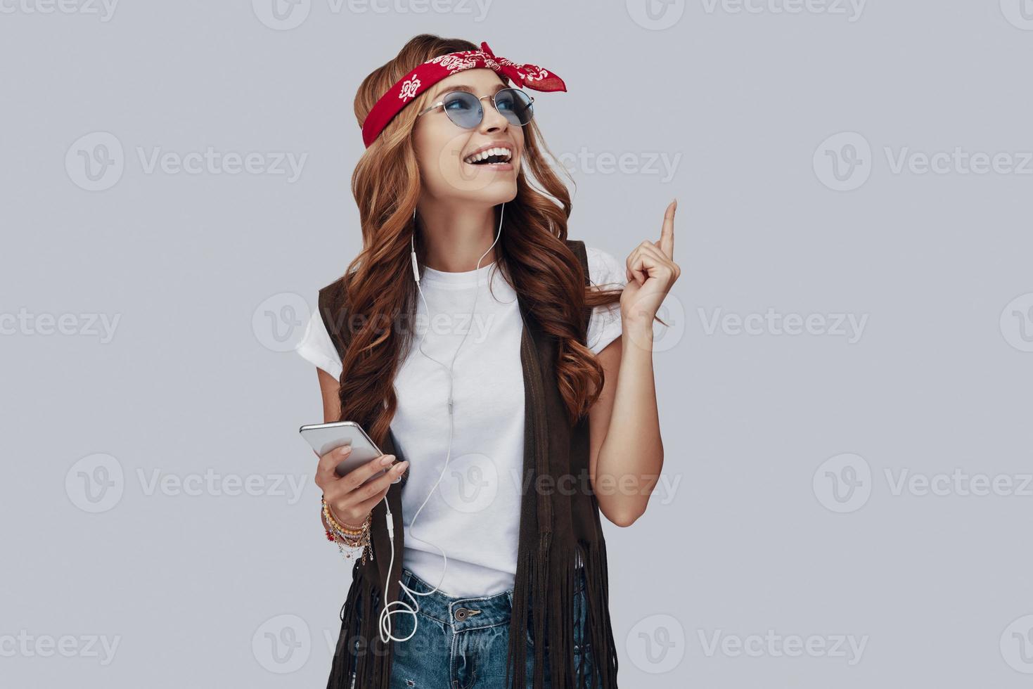 atraente elegante jovem ouvindo música e sorrindo em pé contra um fundo cinza foto