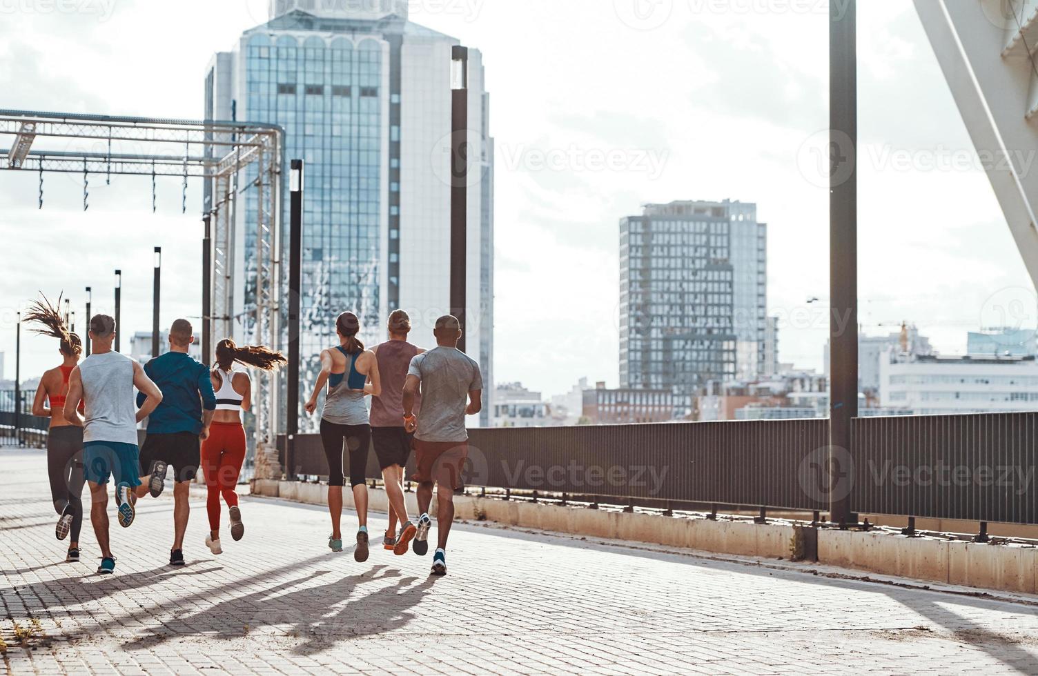 vista traseira de corpo inteiro de pessoas em roupas esportivas correndo enquanto se exercita na calçada ao ar livre foto