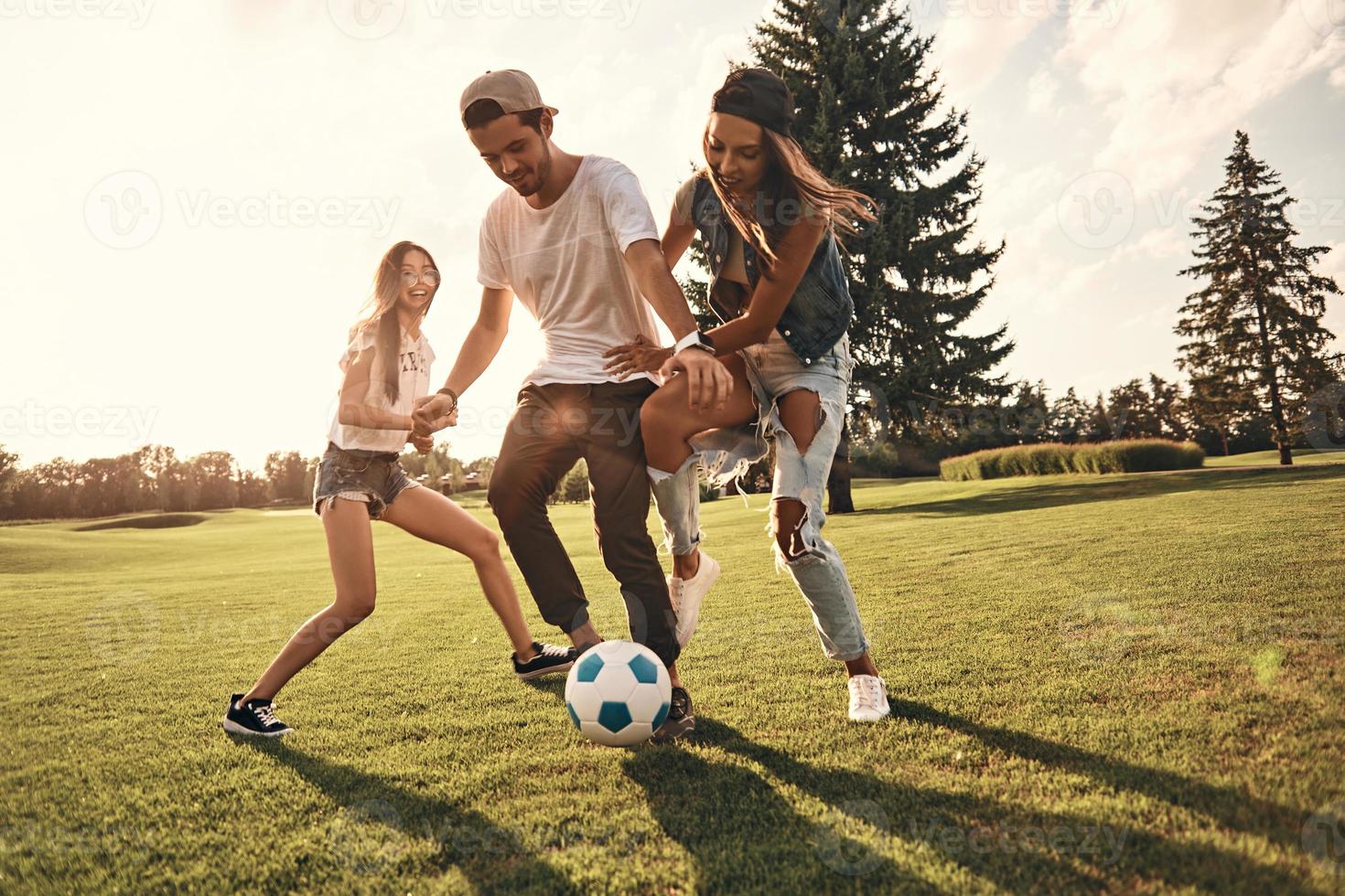 sentindo-se livre com os amigos. comprimento total de jovens sorridentes em roupas casuais correndo enquanto jogava futebol ao ar livre foto