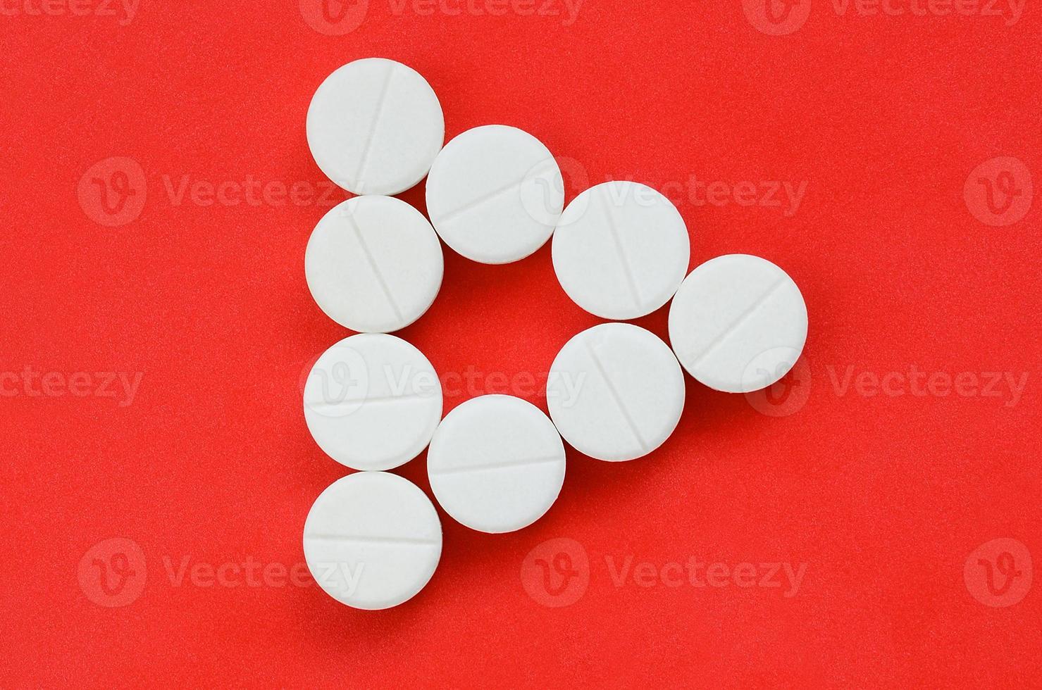 vários comprimidos brancos estão sobre um fundo vermelho brilhante na forma de um triângulo uniforme. imagem de fundo sobre medicina e tópicos farmacêuticos foto
