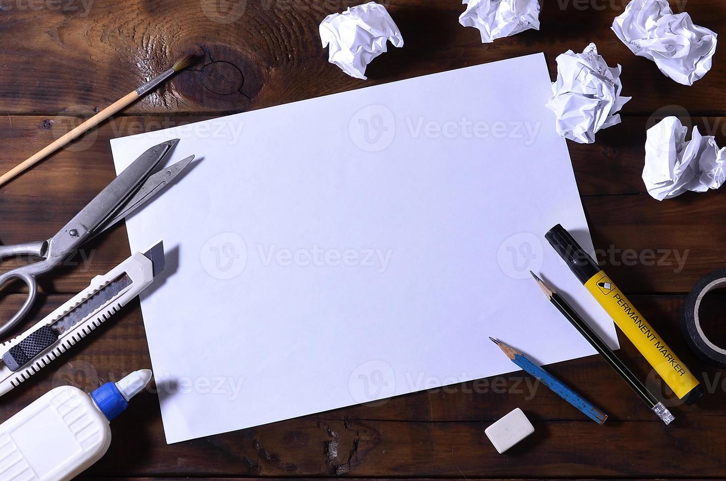 uma escola ou escritório ainda vida com uma folha de papel em branco branca e muitos materiais de escritório. o material escolar está em um fundo de madeira marrom. lugar para texto foto