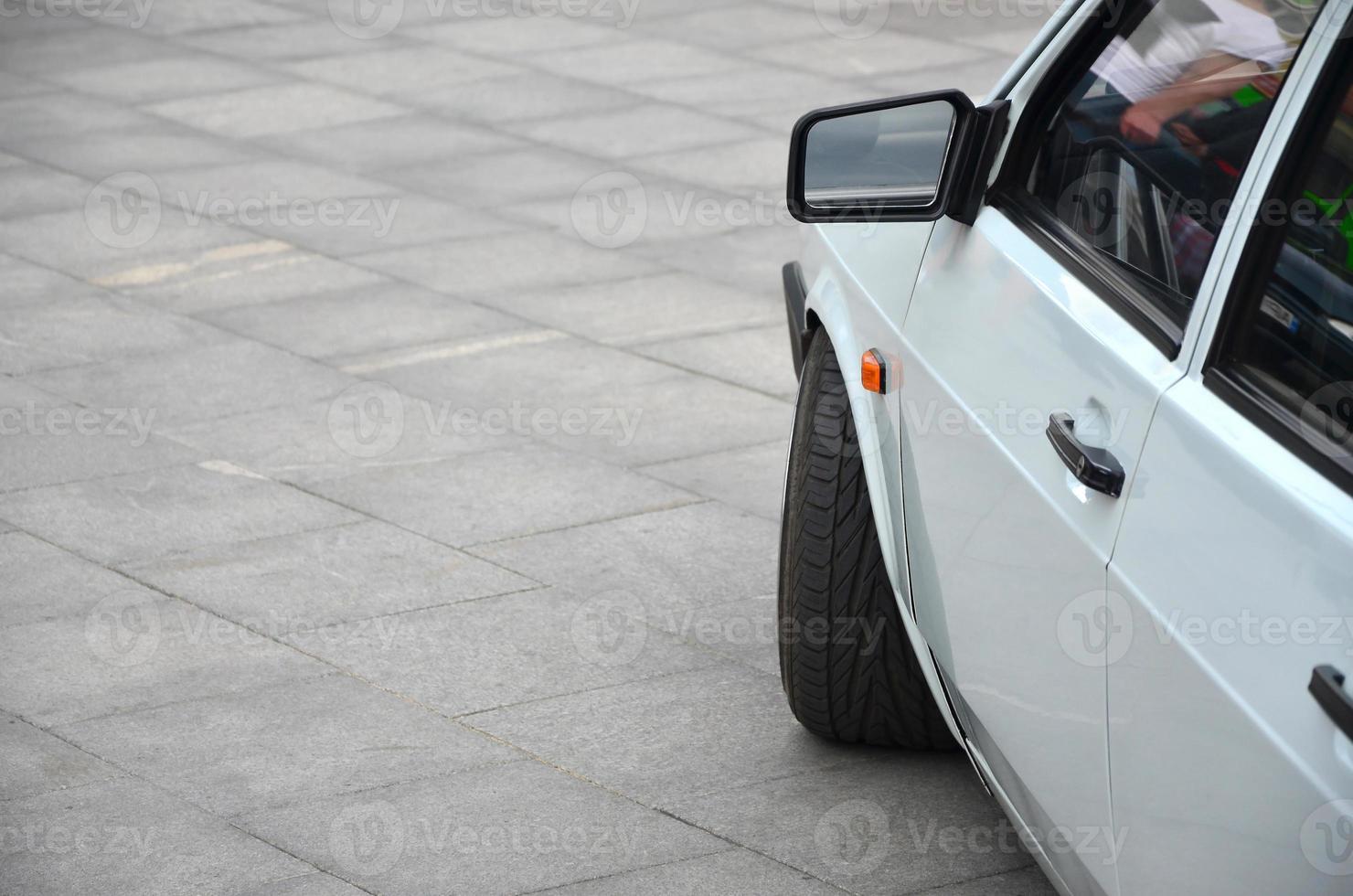 vista diagonal de um carro branco brilhante que fica em um quadrado de azulejos cinza foto