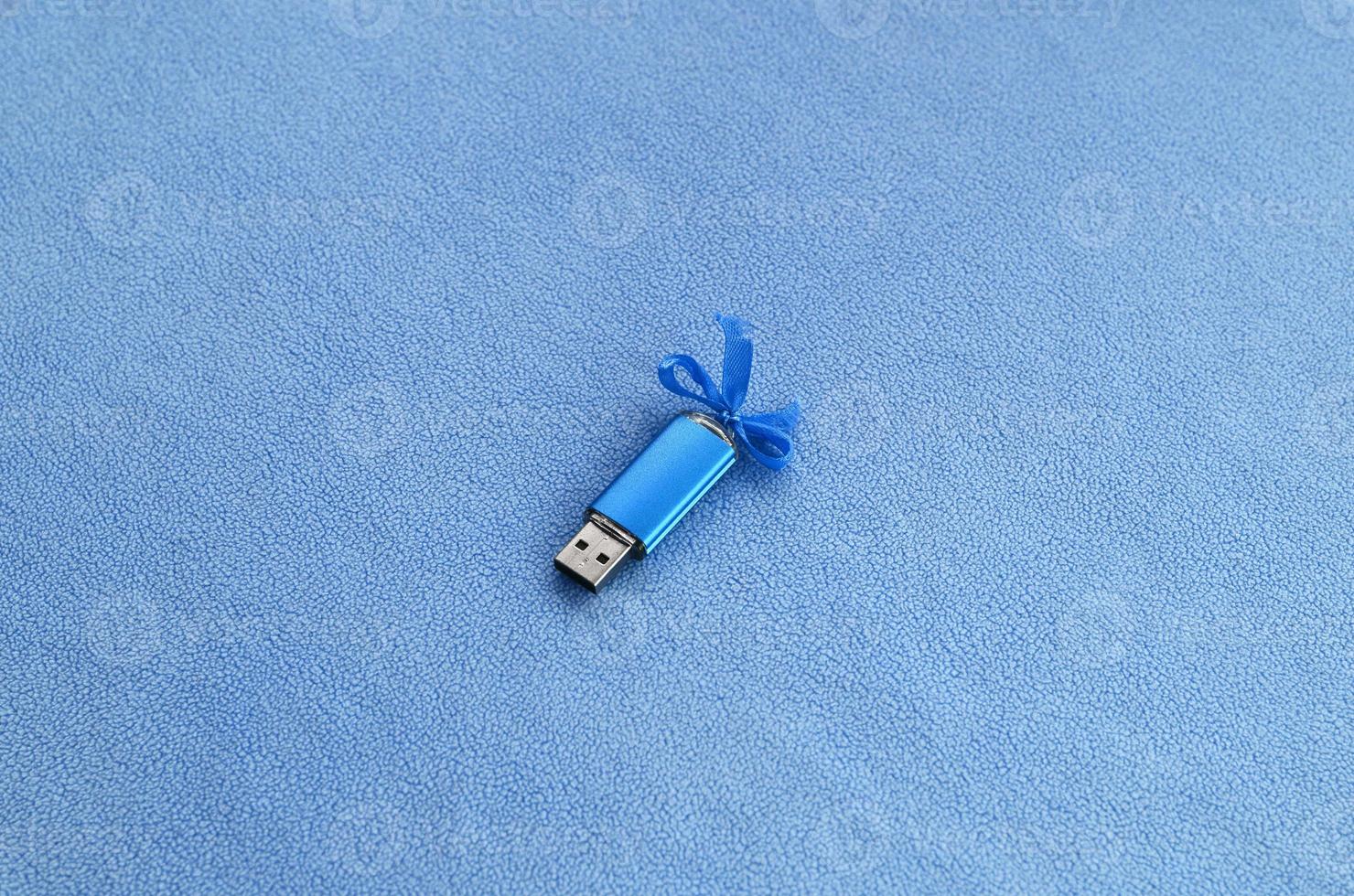 cartão de memória flash usb azul brilhante com um laço azul repousa sobre um cobertor de tecido de lã azul claro macio e peludo. design de presente feminino clássico para um cartão de memória foto
