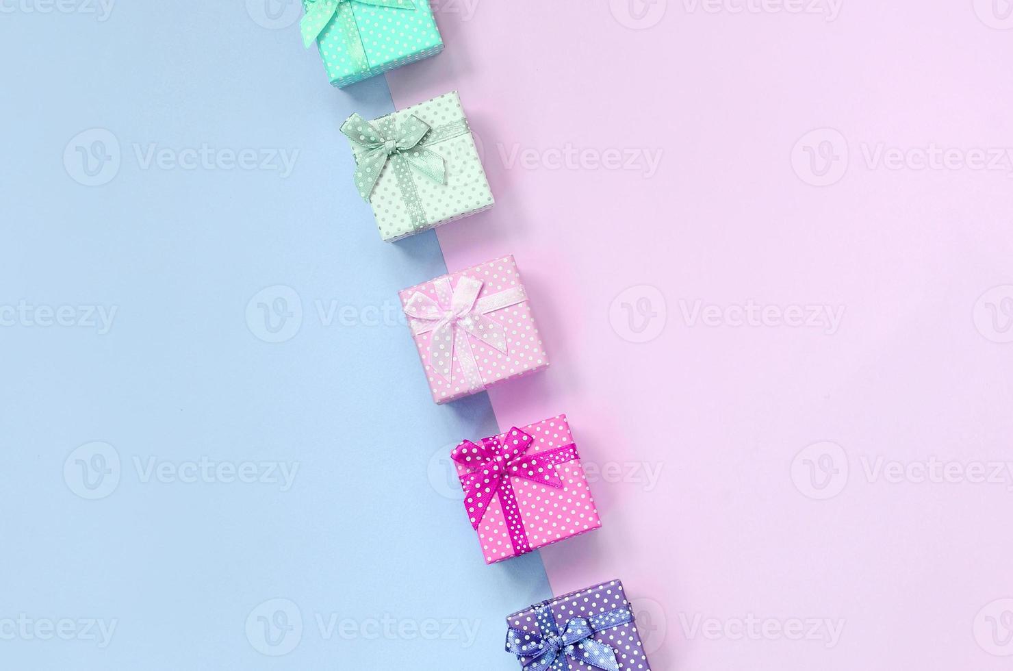 pequenas caixas de presente de cores diferentes com fitas encontram-se em um fundo violeta e rosa foto