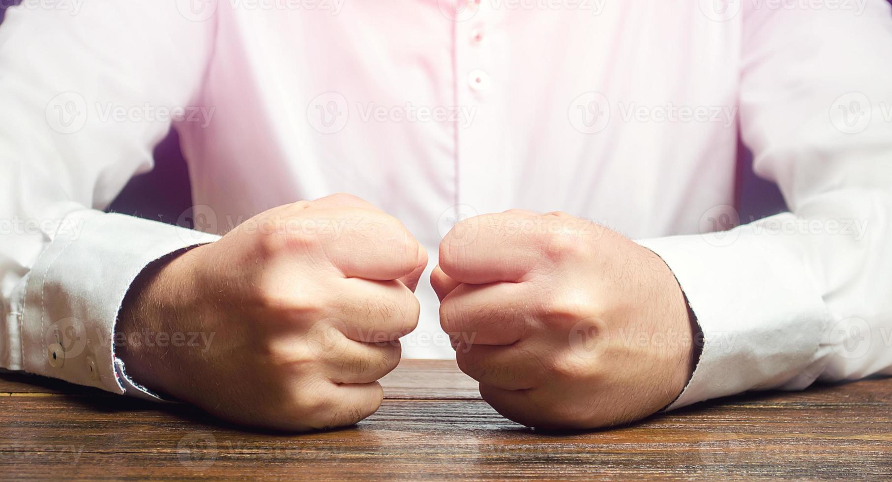 um homem mantém os punhos fechados sobre a mesa. um ataque de raiva, estresse. um gesto decisivo e emocional. homens impulsivos. sofrer derrotas, fracassos e perdas. fim da paciência. é impossível suportar. foto