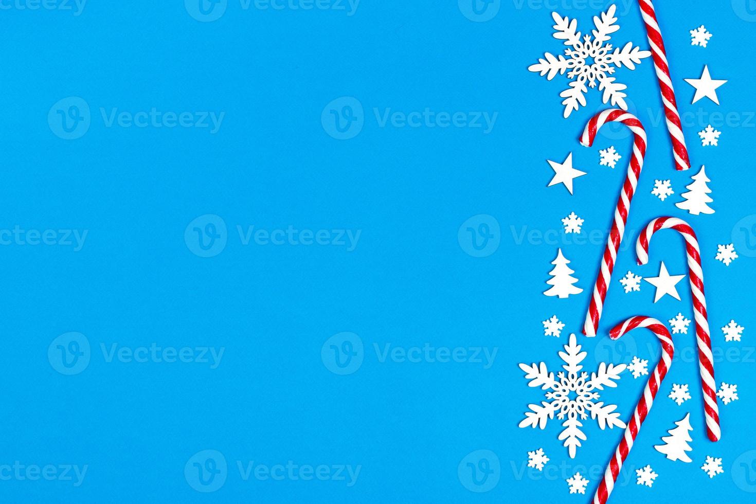 bastão de doces de natal mentiu uniformemente em linha sobre fundo azul com floco de neve decorativo e estrela. postura plana e vista superior foto
