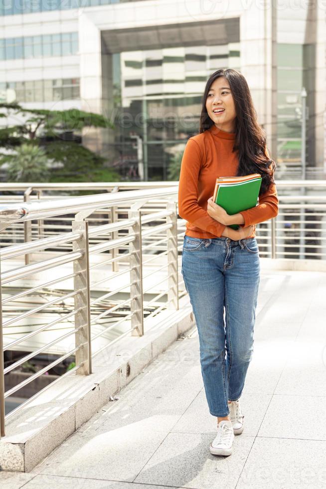 jovem mulher asiática segurando livros e sorrindo na universidade, conceito de educação de pessoas. foto