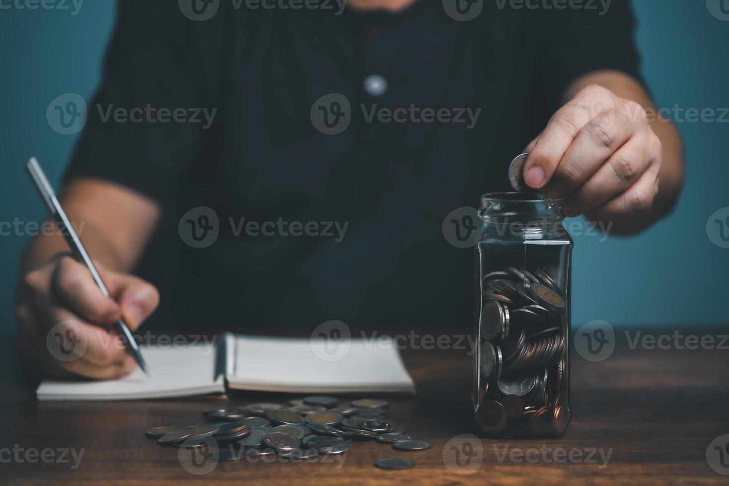 jovem colocando moedas no pote e registrando a quantidade de dinheiro no caderno, economia, caridade, conceito de plano de finanças familiares, captação de recursos, aposentadoria, investimento, conceito de crise financeira. foto