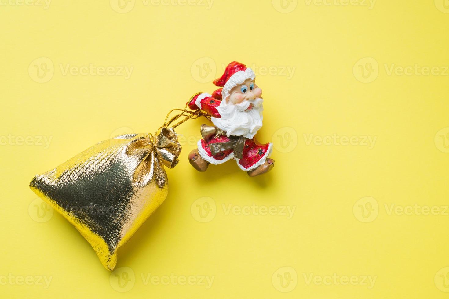 um brinquedo papai noel com um saco de ouro de presentes em fundo amarelo com espaço de cópia. o conceito de natal ano novo. foto