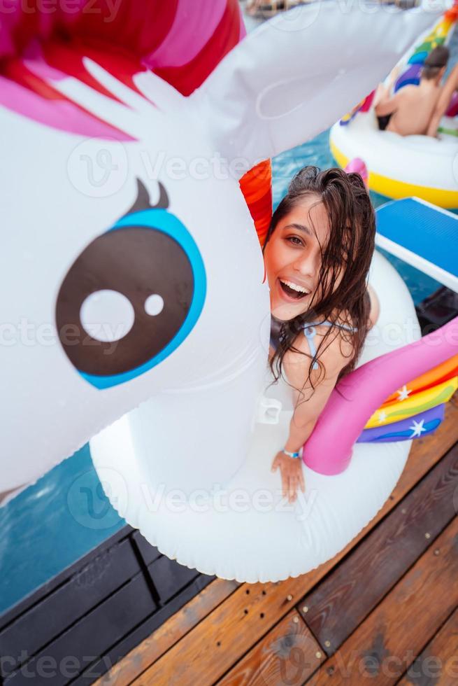 feliz jovem sentada no colchão inflável de brinquedo de unicórnio foto