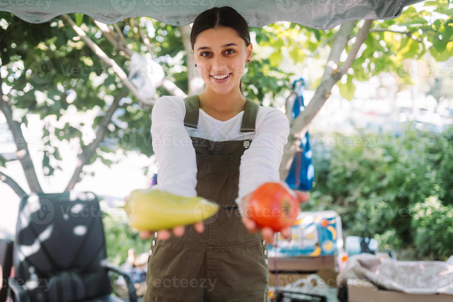 jovem vendedora segurando pimentão e tomate nas mãos foto
