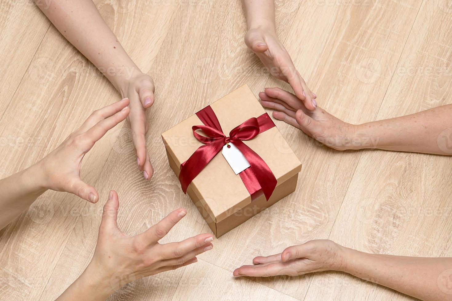 muitas mãos alcançam um presente, uma caixa de presente amarrada com um laço e uma etiqueta vazia foto