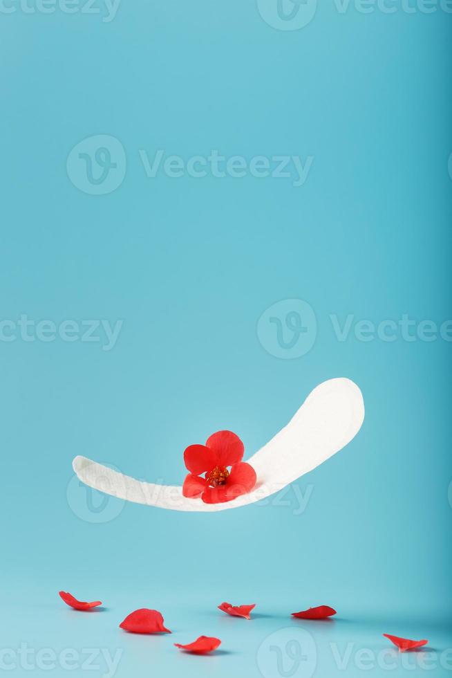absorvente em voo sobre um fundo azul com pétalas caídas de flores vermelhas. conceito do início da menopausa. foto