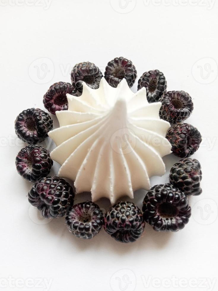 sobremesa de merengue branca decorada com framboesas pretas em um fundo branco foto
