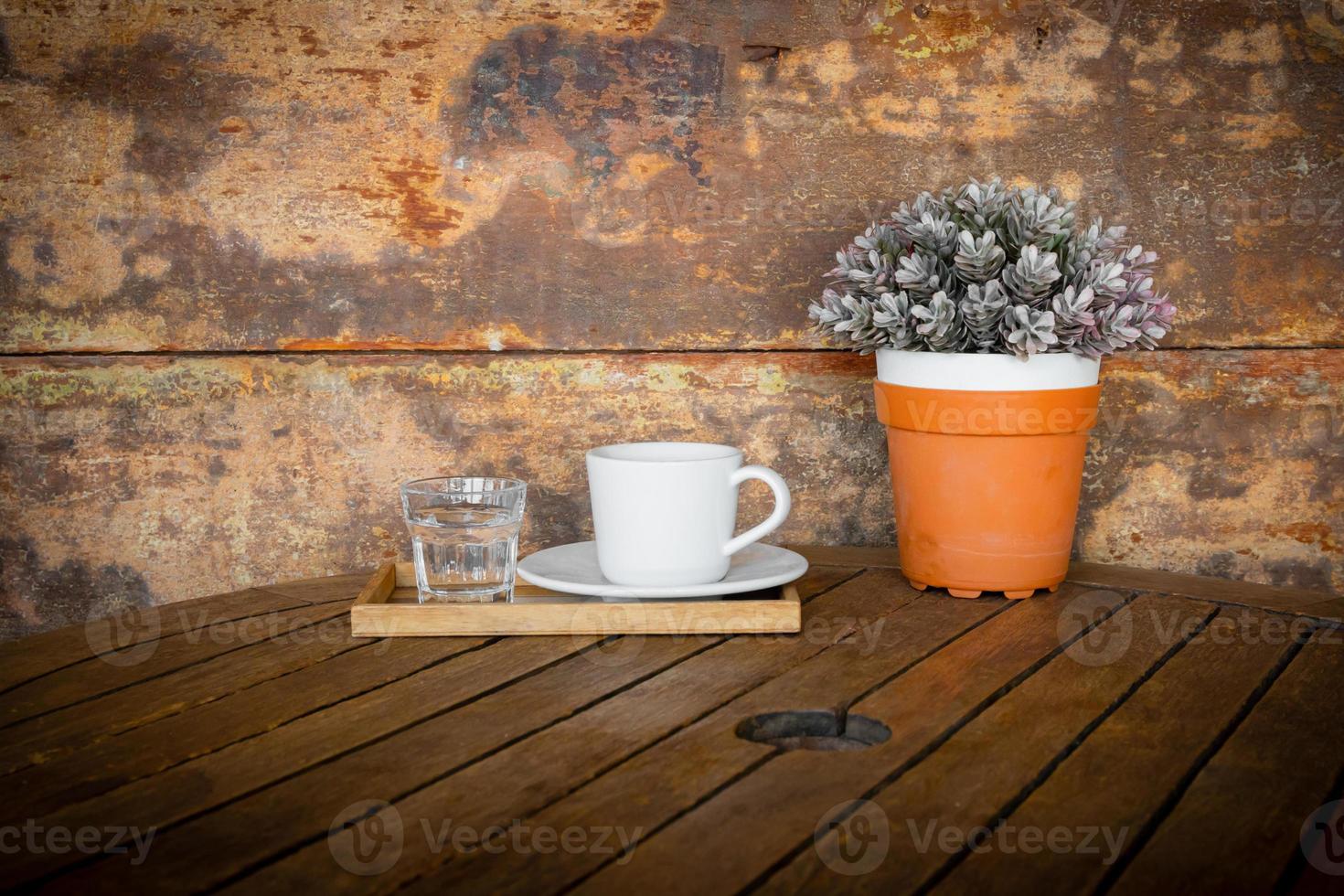 xícara de café branco e copo de água na mesa de madeira vintage e vaso de flores foto
