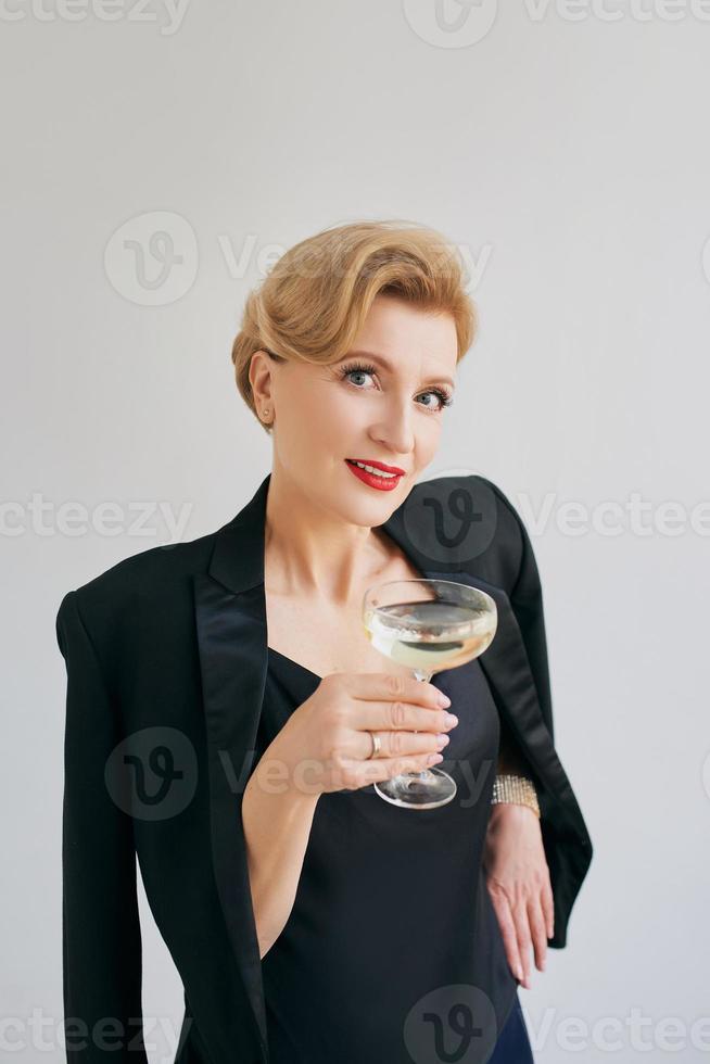 mulher elegante elegante madura de smoking com copo de vinho espumante. festa, celebração, conceito anti-idade foto