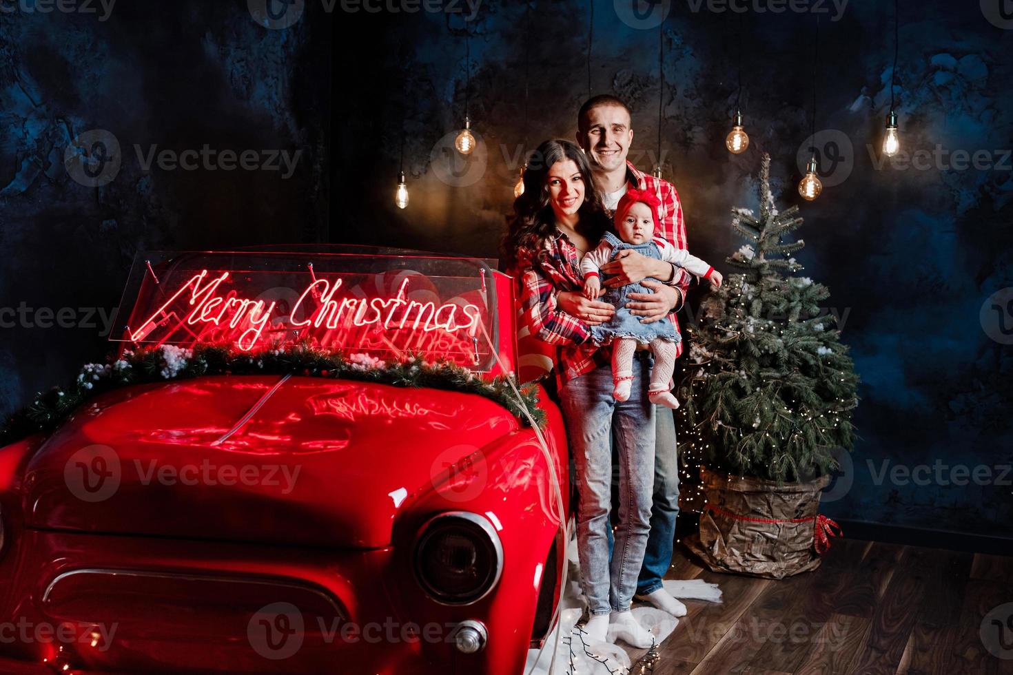 jovens pais lindos segurando sua filha bonita em seus braços se divertindo perto de carro retrô em estúdio. olhar de família de natal. cenário de ano novo. foto